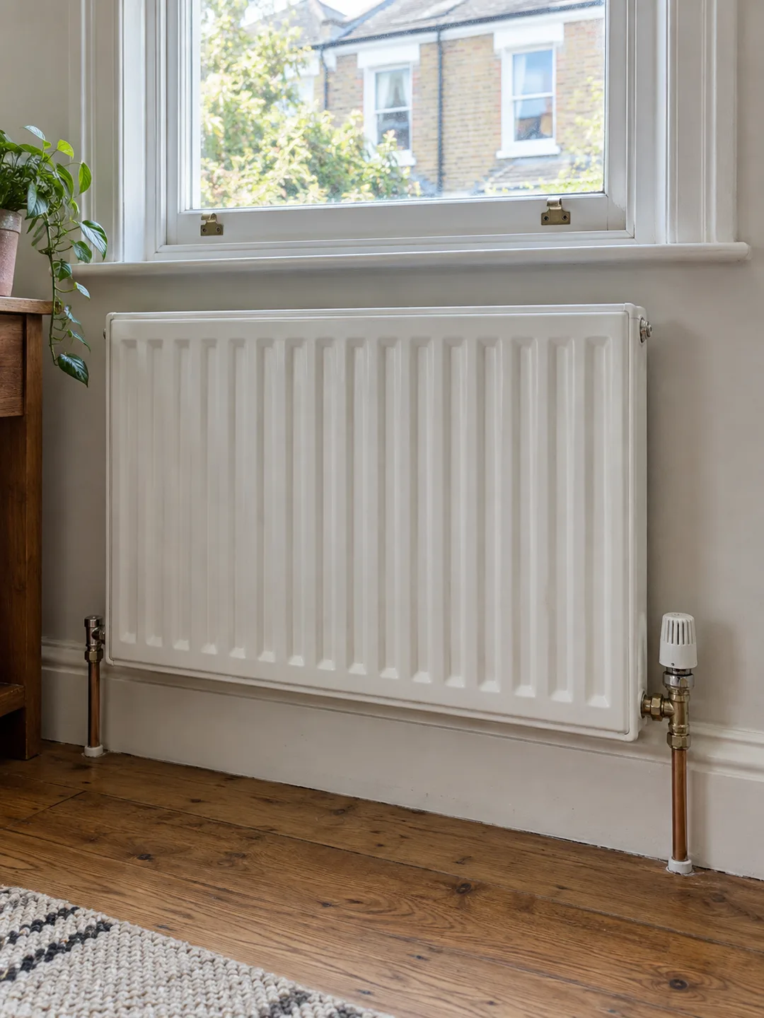 Illustration of a panel radiator and thermostatic valve beneath a window